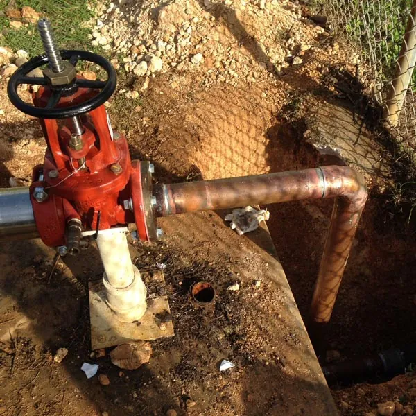 A backflow preventer install by Barrett: a red shut-off valve on copper pipe in a dug-out trench
