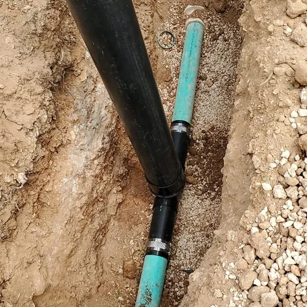 Black sewer pipe joined to a green line in an open trench